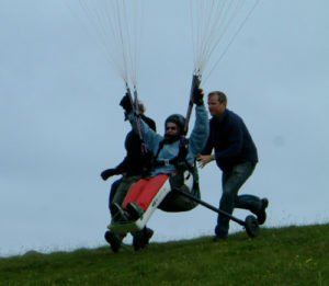 A sanderson paragliding wheelchair being flown solo launched by 2 assistants