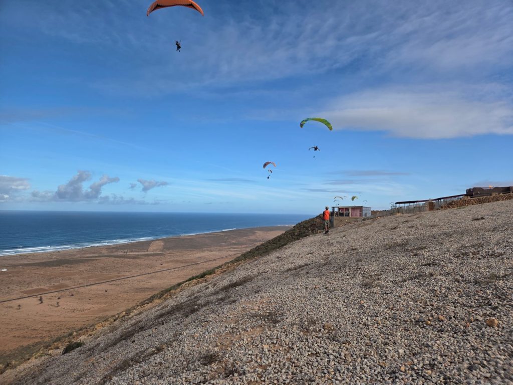 Michael under the green/blue wing orange helmet flying in Morocco with Mid-Wales ParaGliding Centre , being carefully watched by 0Steve